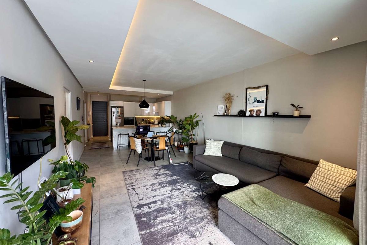 Modern open-plan living area featuring tiled floors, recessed cove lighting, and a sleek kitchen with built-in appliances and a central island.