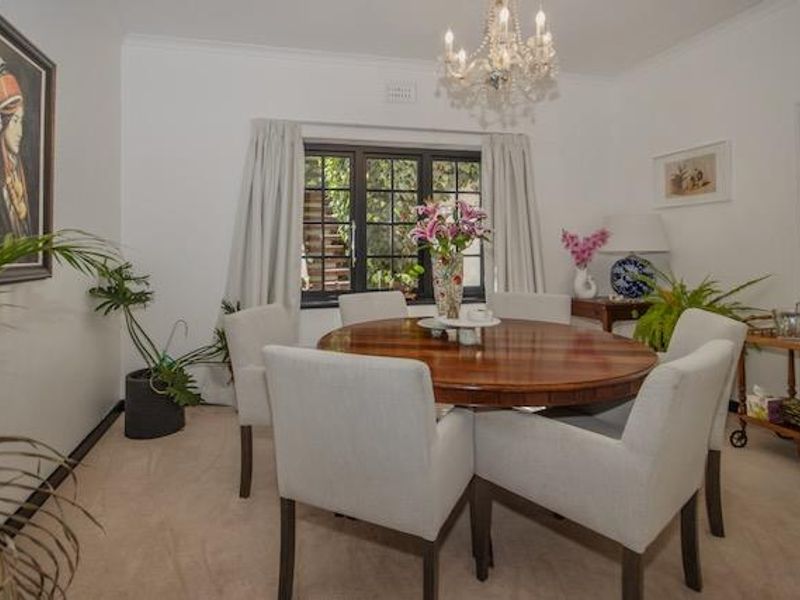 A well-lit dining room featuring a classic chandelier, neutral carpeting, and a window overlooking the exterior.