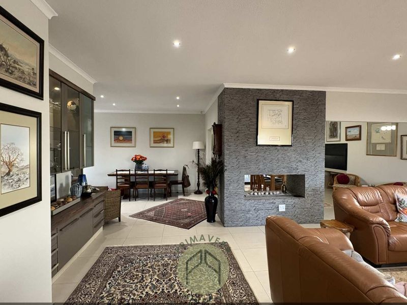 Spacious open-plan living and dining area featuring a central stone-clad fireplace, recessed lighting, and modern tiled flooring.