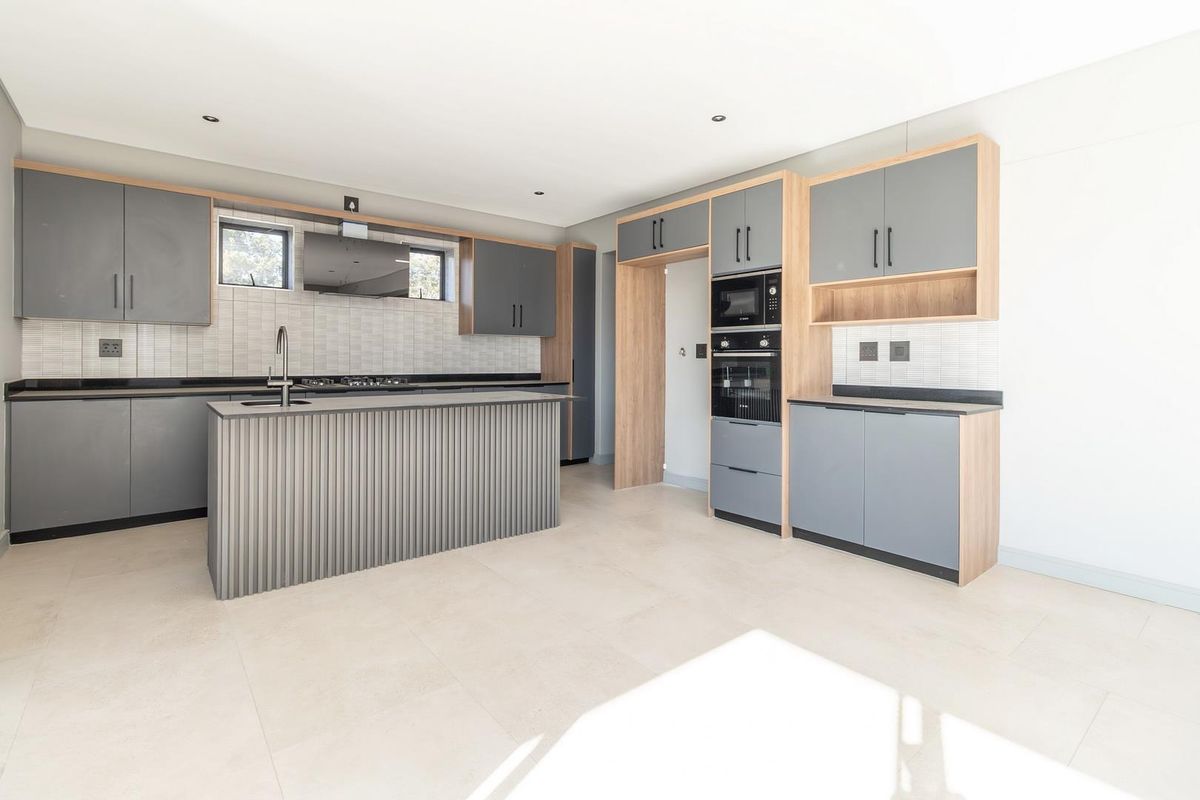 Modern kitchen featuring grey cabinetry, wood-tone accents, a central island with sink, built-in oven, microwave, and tiled backsplash.