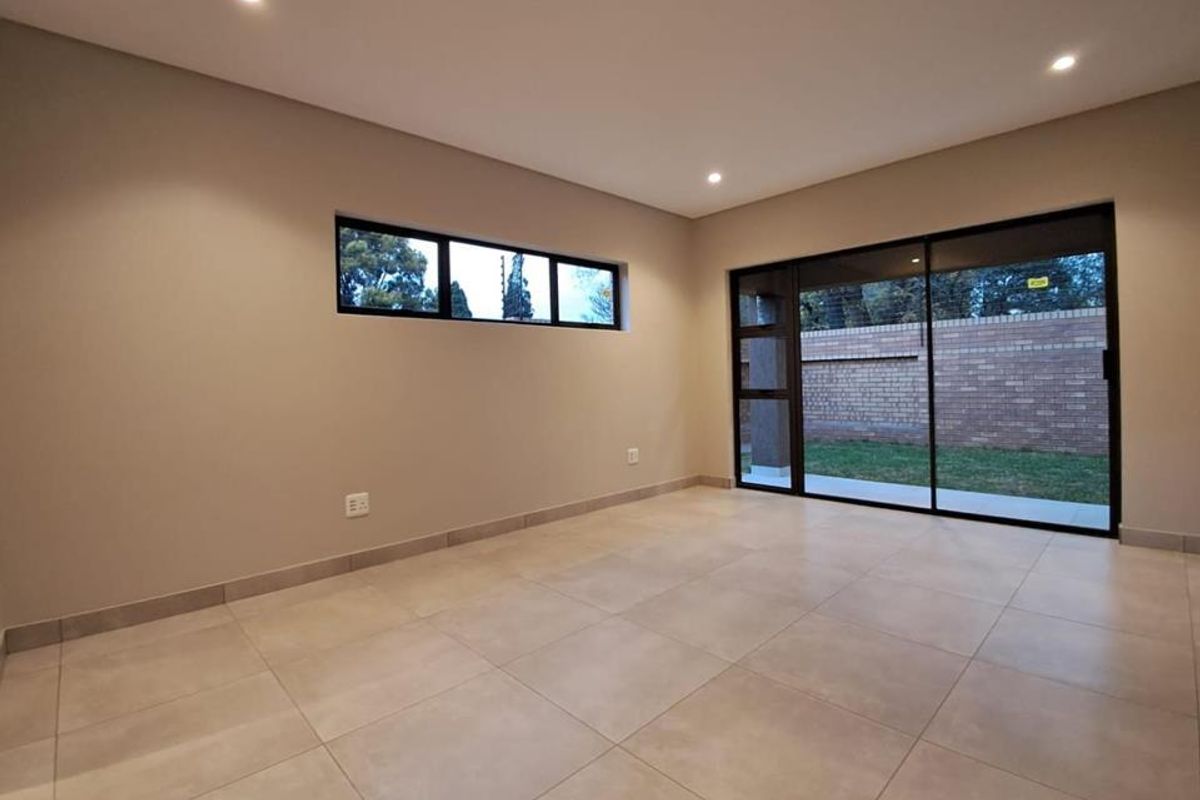 A bright, modern living area featuring large format floor tiles, recessed downlighting, and expansive sliding glass doors providing direct access to the rear garden.