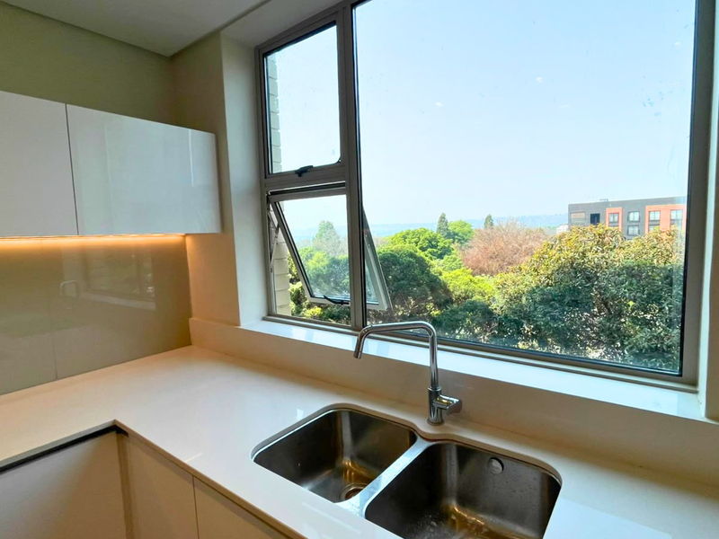 Modern kitchen area featuring sleek white cabinetry, quartz countertops, a double stainless steel sink, and a large window with a pleasant green outlook.