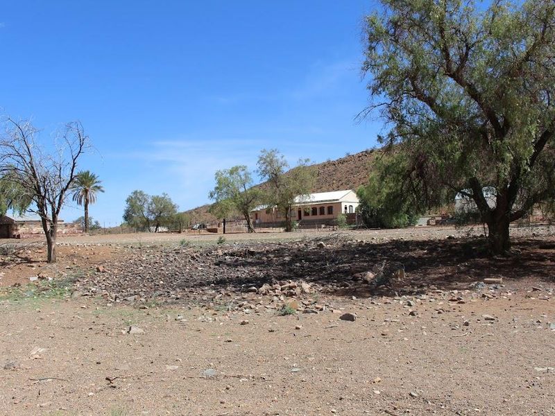 A wide-angle view of the farm property featuring the main farmhouse, surrounding outbuildings, and expansive arid landscape.