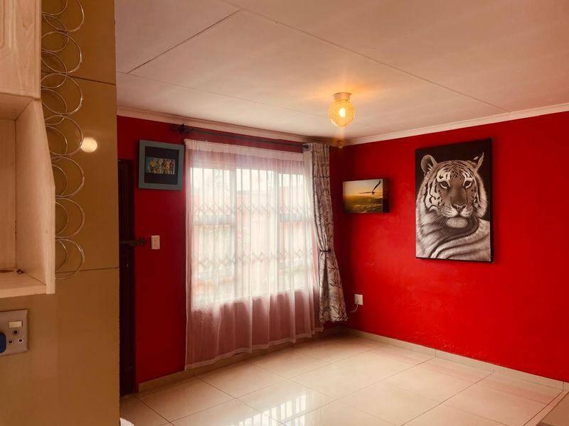 A living area featuring tiled flooring, a ceiling light fixture, and a window fitted with a security gate.