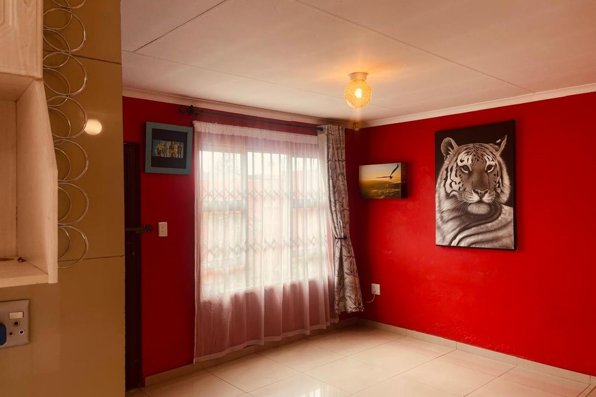 A living area featuring tiled flooring, a ceiling light fixture, and a window fitted with a security gate.