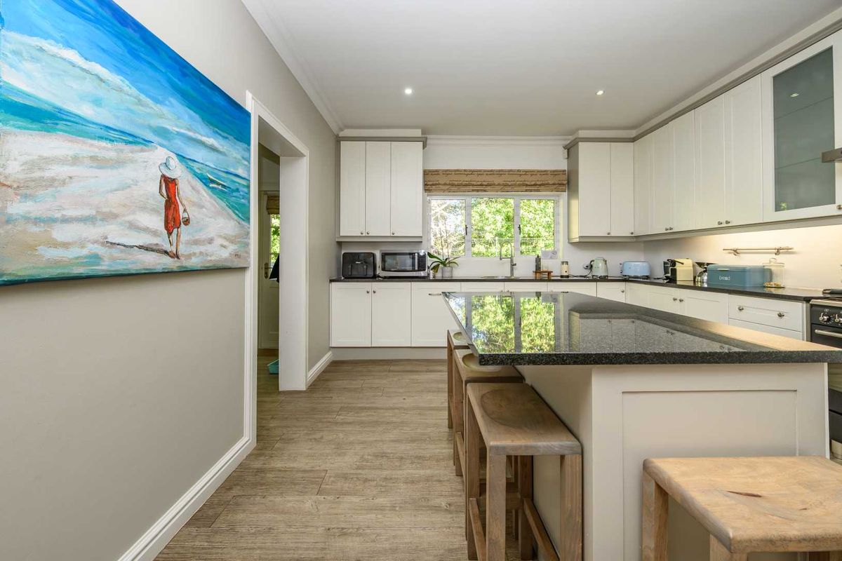A modern kitchen featuring white cabinetry, dark granite countertops, a central island with breakfast bar seating, and wood-look flooring.
