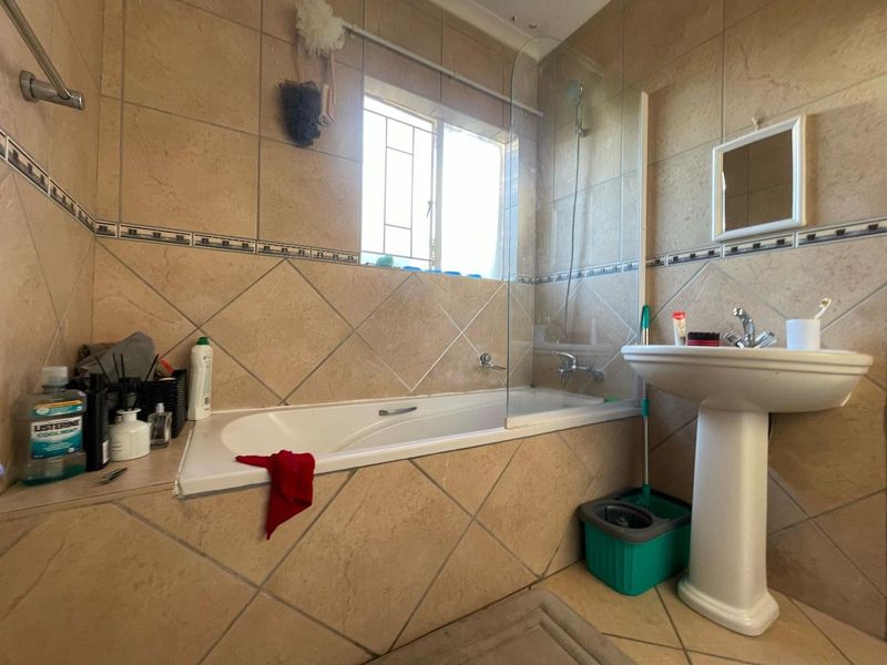 A functional bathroom featuring a built-in bathtub with a glass shower screen, pedestal basin, and neutral ceramic tiling throughout.