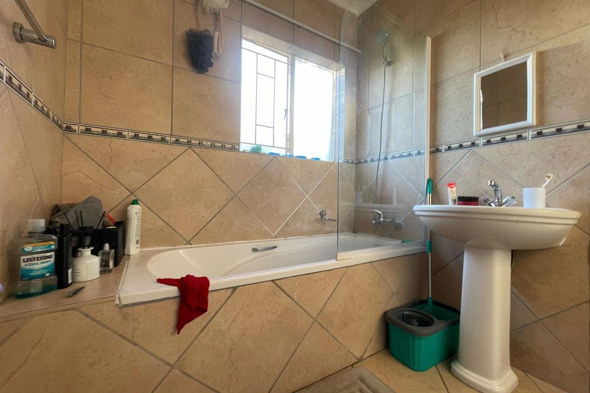 A functional bathroom featuring a built-in bathtub with a glass shower screen, pedestal basin, and neutral ceramic tiling throughout.