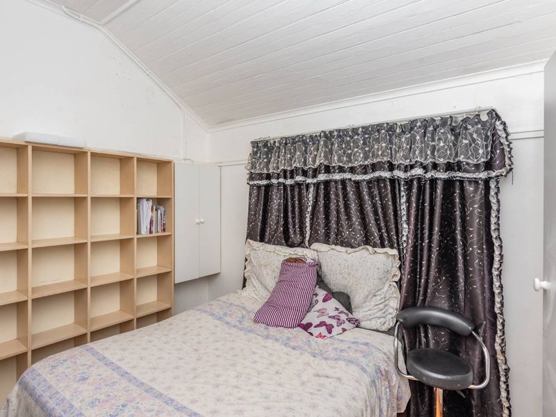 A bedroom featuring a vaulted timber ceiling, built-in shelving, and a built-in cupboard, offering potential for a modern update.