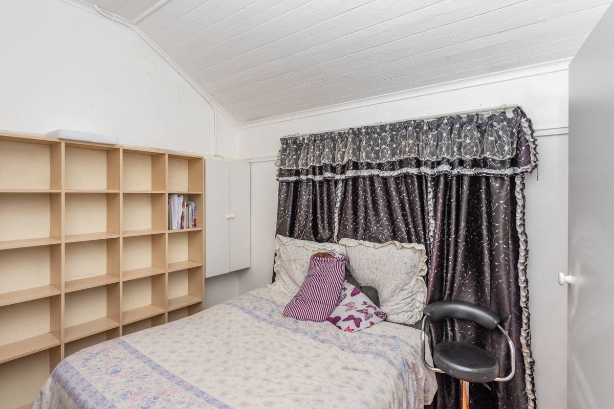 A bedroom featuring a vaulted timber ceiling, built-in shelving, and a built-in cupboard, offering potential for a modern update.