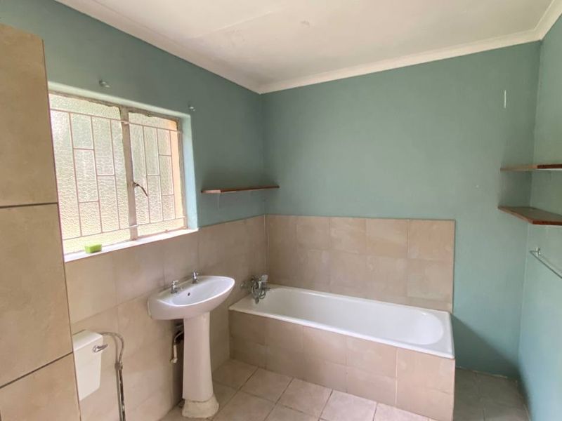 A functional bathroom featuring a pedestal basin, built-in bathtub, and tiled finishes, offering a blank canvas for potential modernization and renovation.