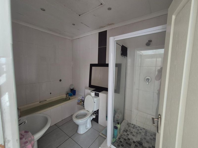 A functional bathroom featuring a bathtub, separate shower enclosure, toilet, and pedestal basin, requiring some maintenance to the ceiling and finishes.