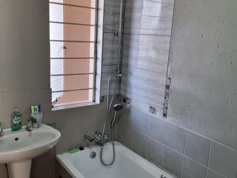 Bathroom featuring a pedestal basin and a bathtub with a shower mixer. The wall tiling is incomplete and requires finishing.
