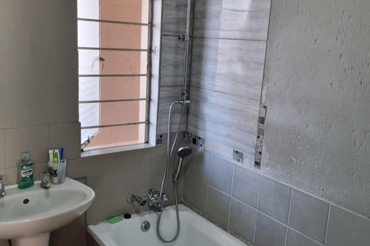 Bathroom featuring a pedestal basin and a bathtub with a shower mixer. The wall tiling is incomplete and requires finishing.