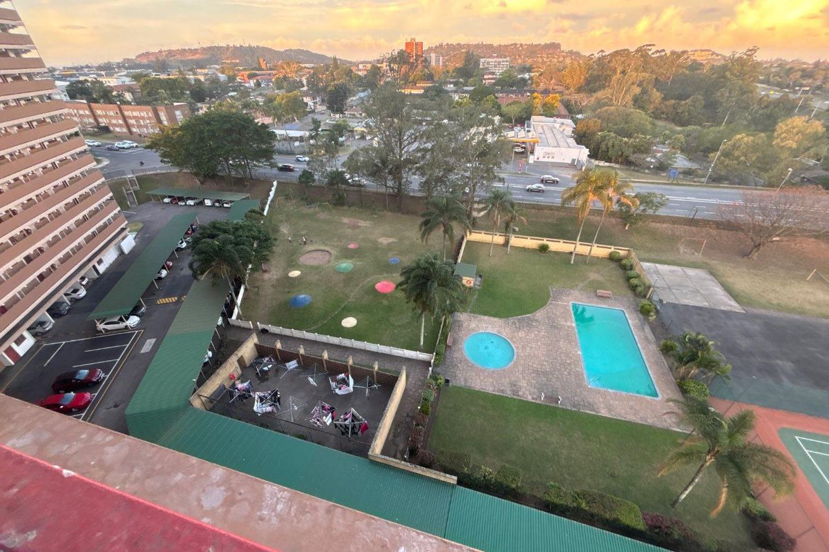 Aerial view of the apartment complex grounds featuring a swimming pool, wading pool, landscaped gardens, tennis court, and covered parking facilities.