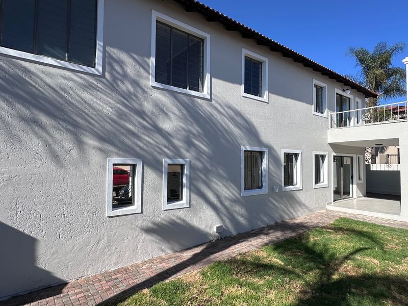 Rear exterior view of the two-story house featuring a paved walkway, balcony, and multiple windows with security bars.