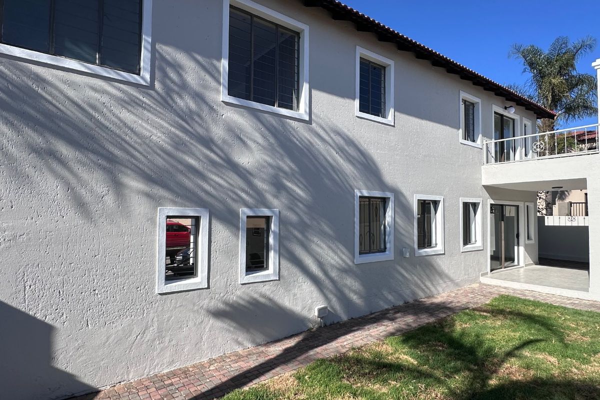 Rear exterior view of the two-story house featuring a paved walkway, balcony, and multiple windows with security bars.