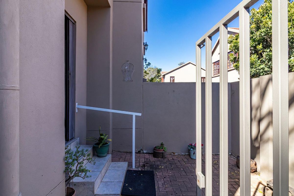 A private paved rear courtyard featuring a metal gate, tiled steps with a handrail, and high boundary walls for added privacy.