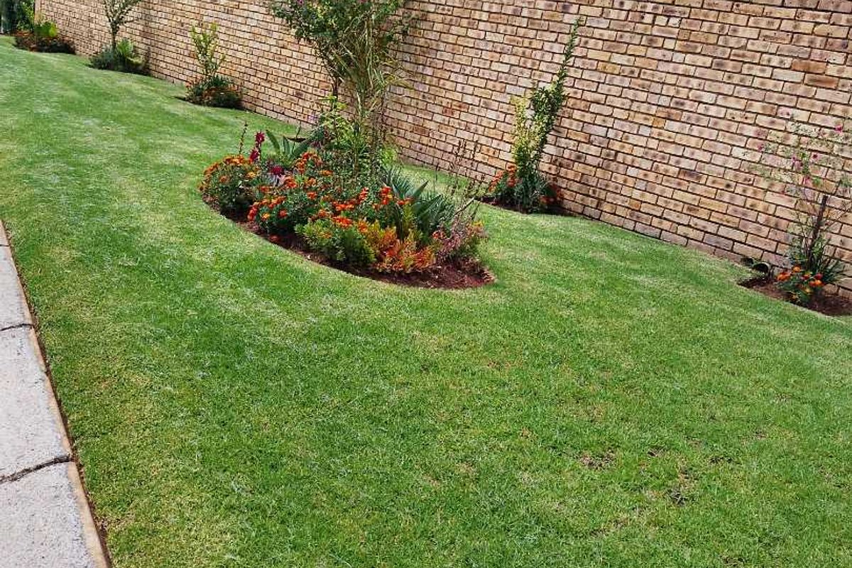 A well-maintained side garden featuring a neat lawn, landscaped flower beds, and a sturdy brick boundary wall.