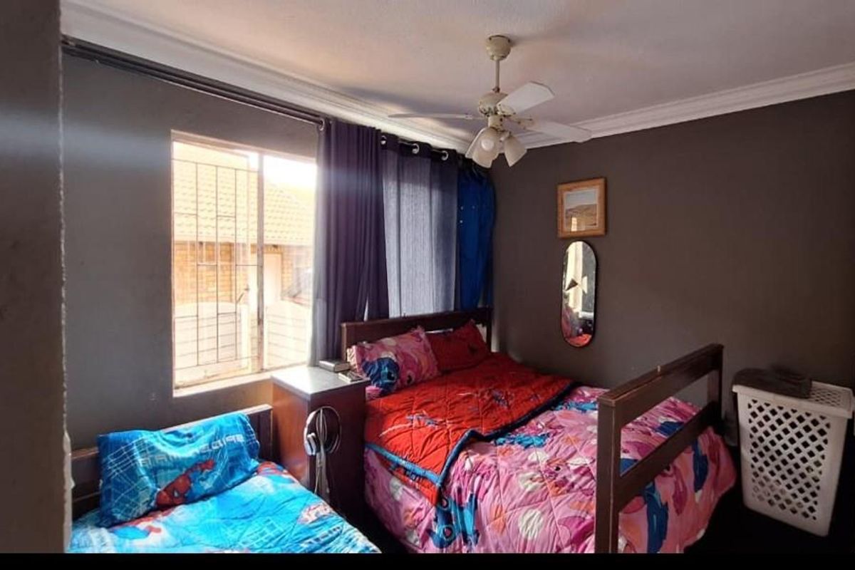 A bedroom featuring a ceiling fan, security bars on the window, and dark-toned walls, providing a functional sleeping space.