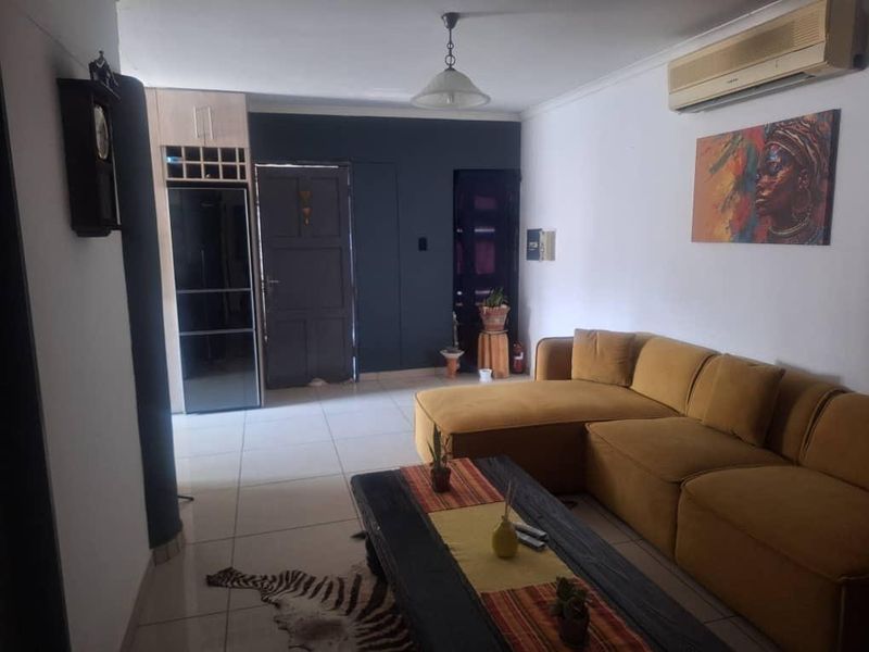 A living room featuring tiled flooring, a wall-mounted air conditioning unit, and built-in cabinetry, providing a functional and comfortable living space.
