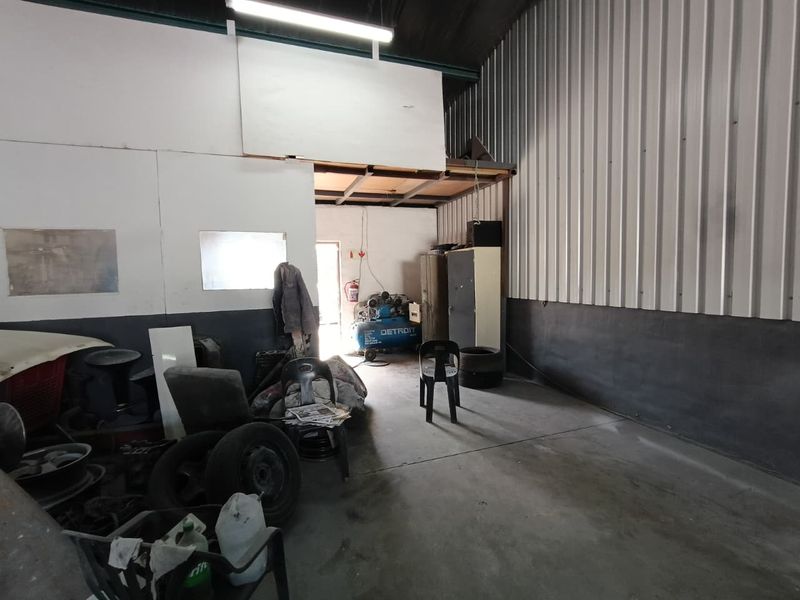 Industrial utility space featuring high ceilings, corrugated metal wall cladding, concrete flooring, and a mezzanine storage level, suitable for workshop or storage use.