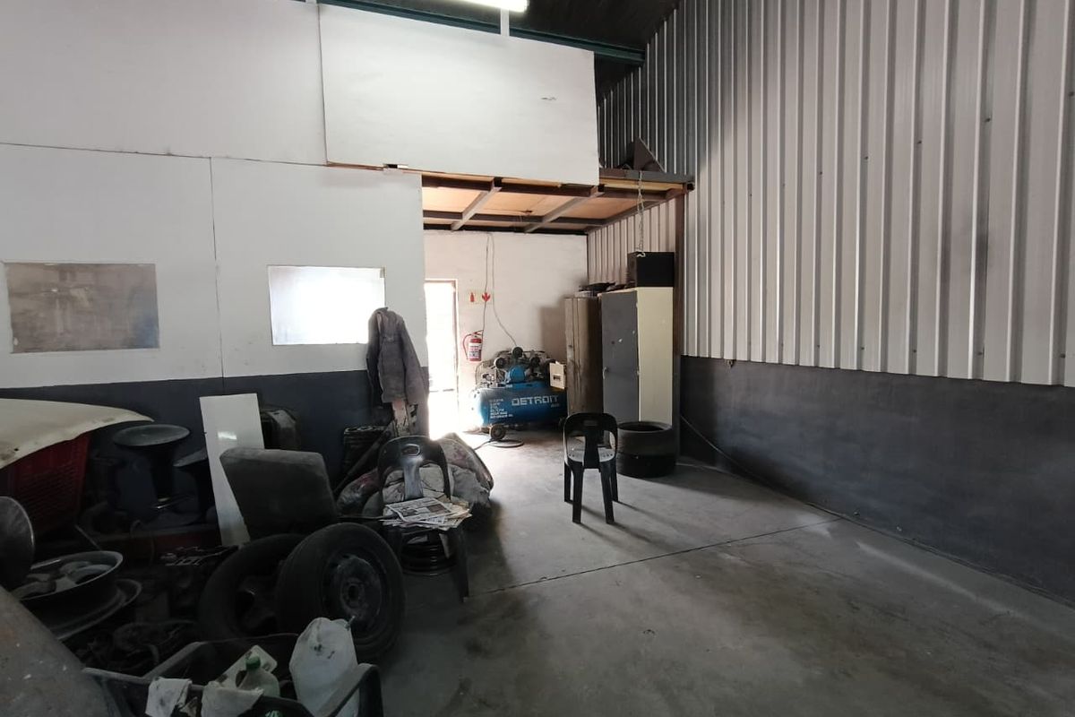 Industrial utility space featuring high ceilings, corrugated metal wall cladding, concrete flooring, and a mezzanine storage level, suitable for workshop or storage use.