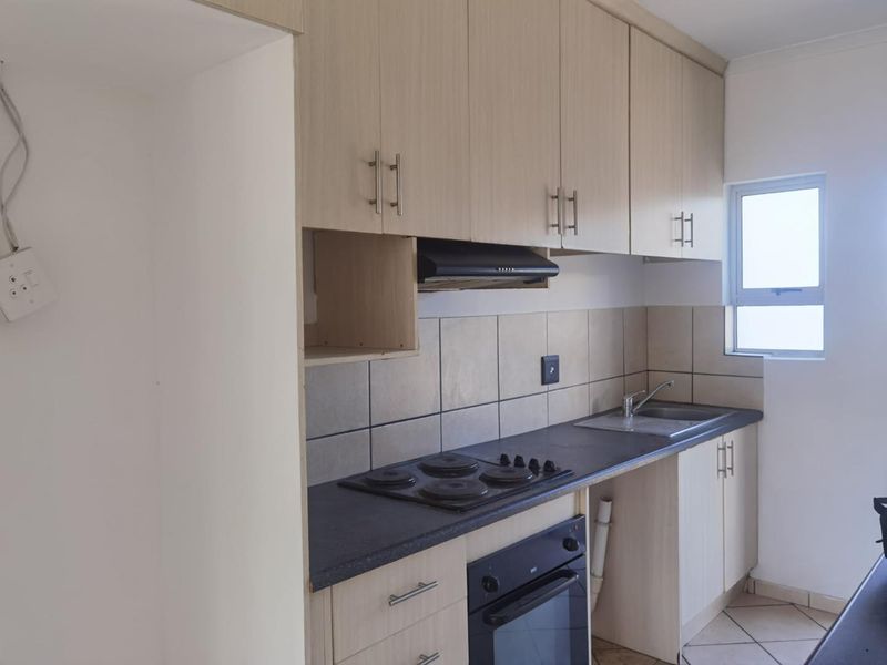 A functional kitchen featuring light wood-finish cabinetry, a built-in oven and hob, tiled splashbacks, and a stainless steel sink.