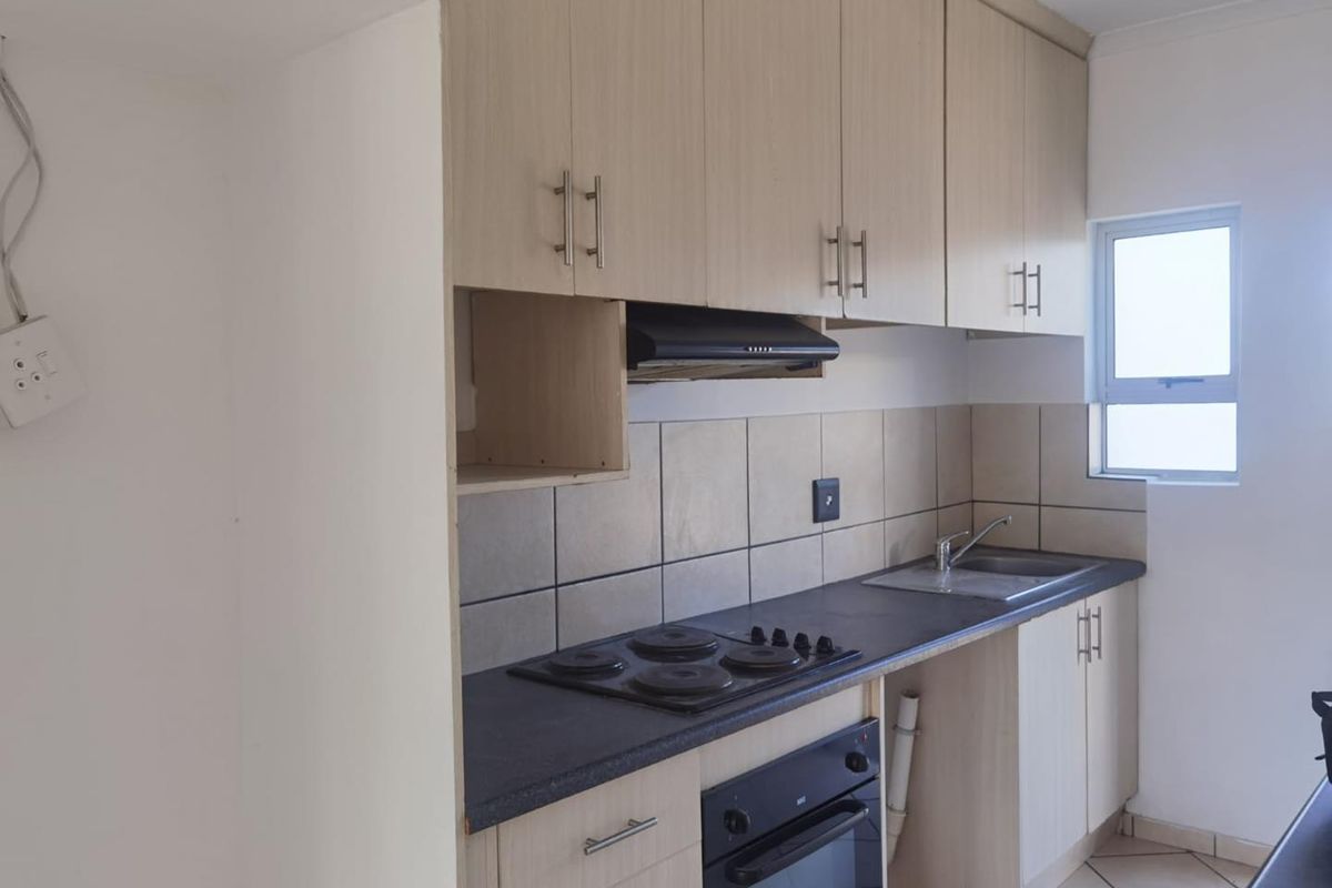 A functional kitchen featuring light wood-finish cabinetry, a built-in oven and hob, tiled splashbacks, and a stainless steel sink.