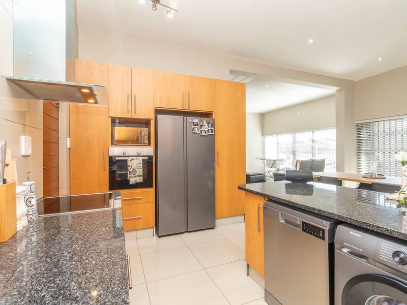 Modern kitchen featuring granite countertops, wooden cabinetry, built-in oven, extractor fan, and integrated appliances, flowing into an open-plan living area.