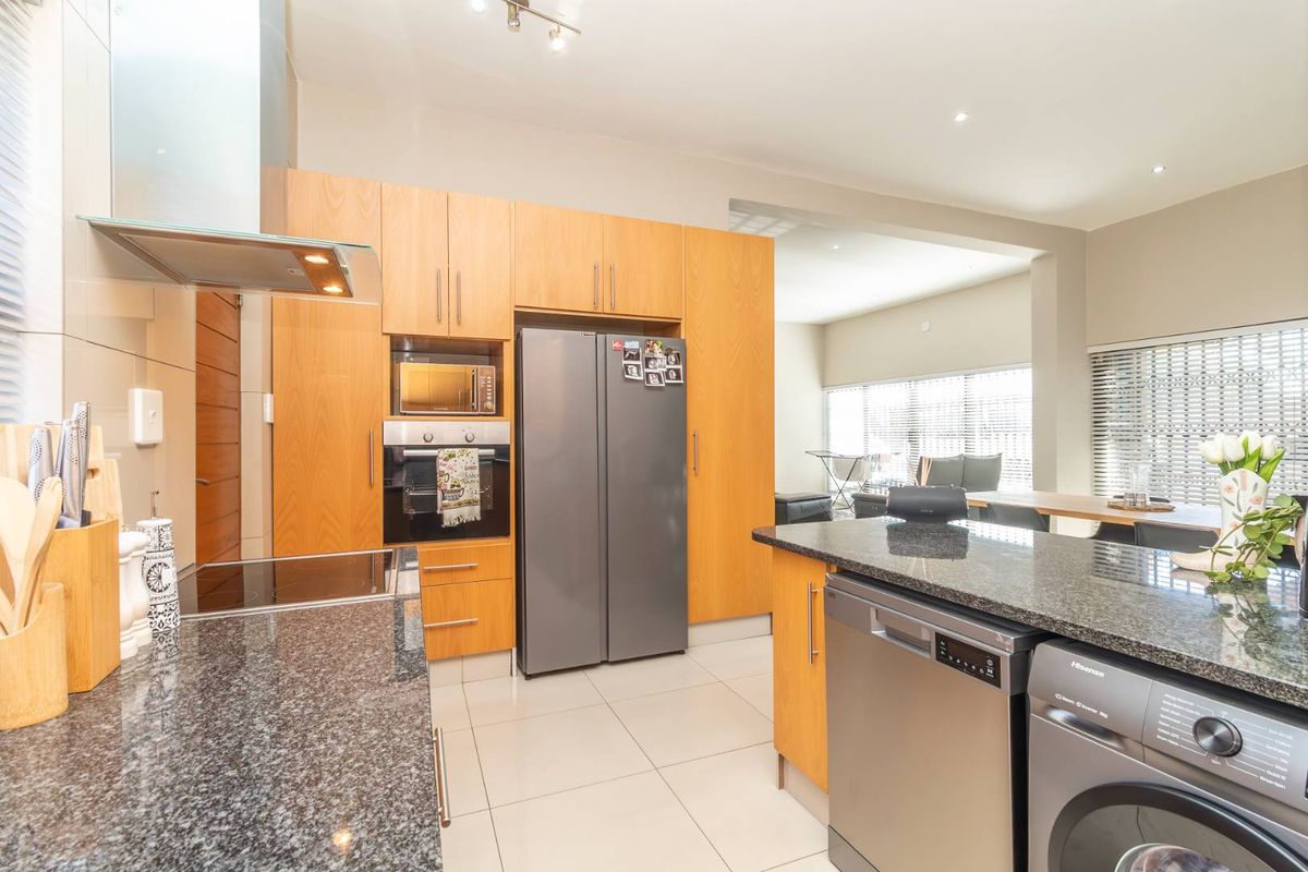 Modern kitchen featuring granite countertops, wooden cabinetry, built-in oven, extractor fan, and integrated appliances, flowing into an open-plan living area.