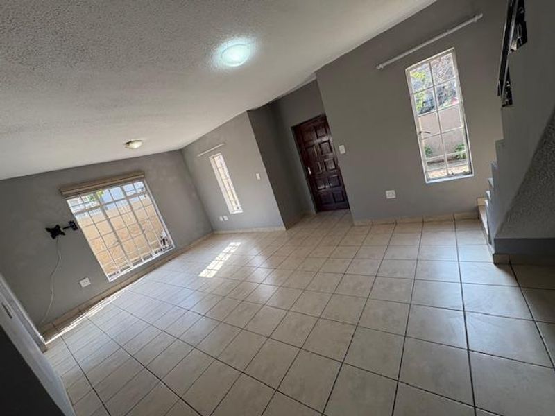 An empty, open-plan living area featuring neutral grey walls, tiled flooring, and a staircase leading to the upper level.