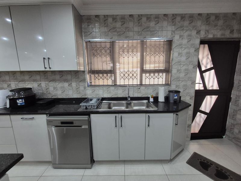 A functional kitchen featuring modern white cabinetry, dark granite countertops, a double basin sink, and a tiled backsplash with an adjacent exterior door.