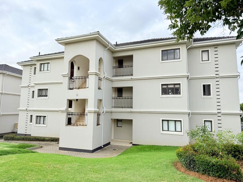 A well-maintained multi-story apartment building exterior featuring neutral rendered walls, dark aluminium window frames, and wrought iron balcony railings.