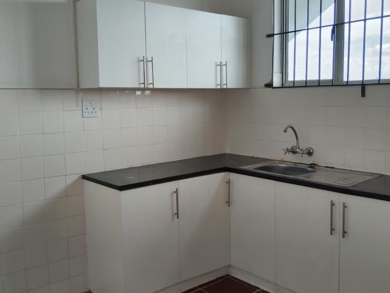 A functional kitchen featuring white built-in cabinetry, dark laminate countertops, a stainless steel sink, and tiled flooring with a window security grill.
