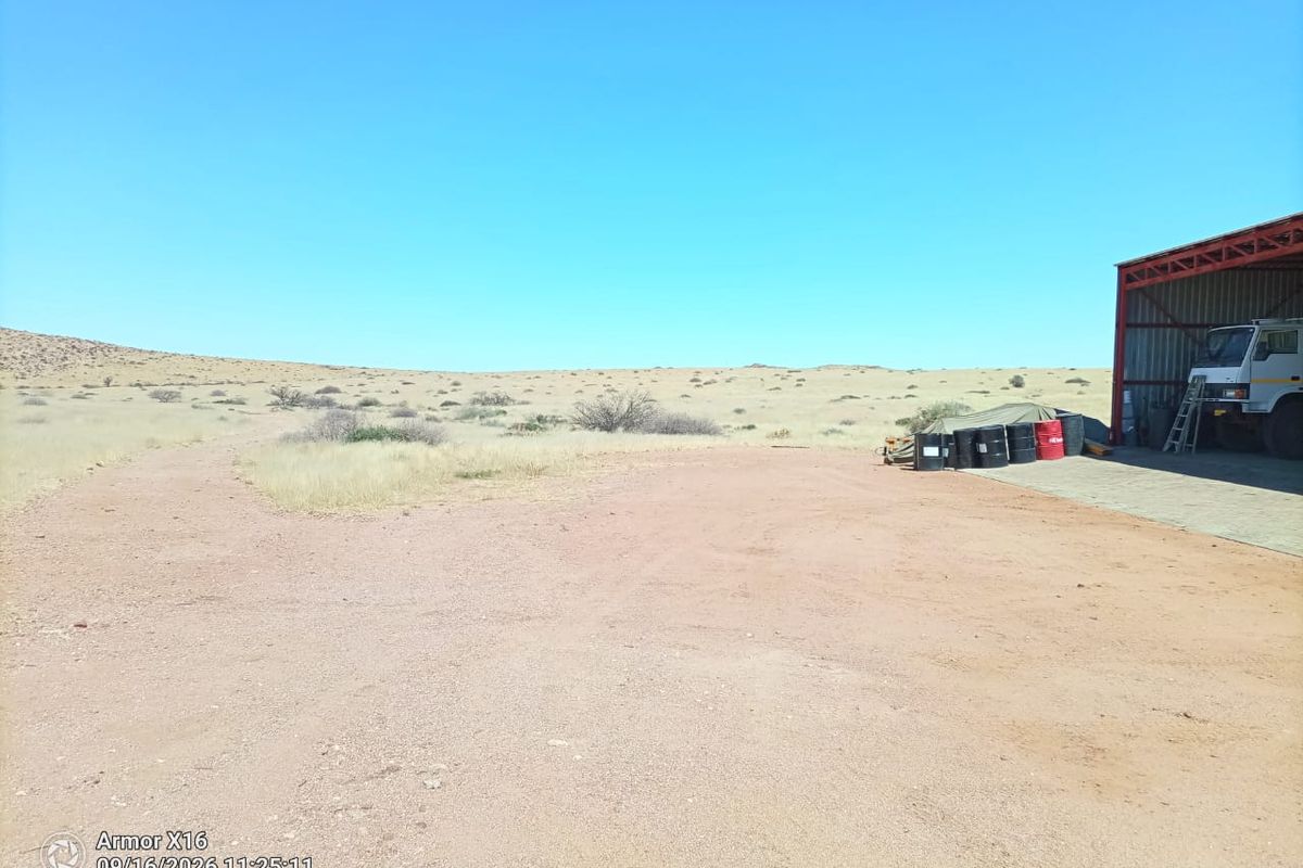 A view of a large steel-framed farm shed with a concrete apron, situated on a vast, arid landscape with a dirt access road.