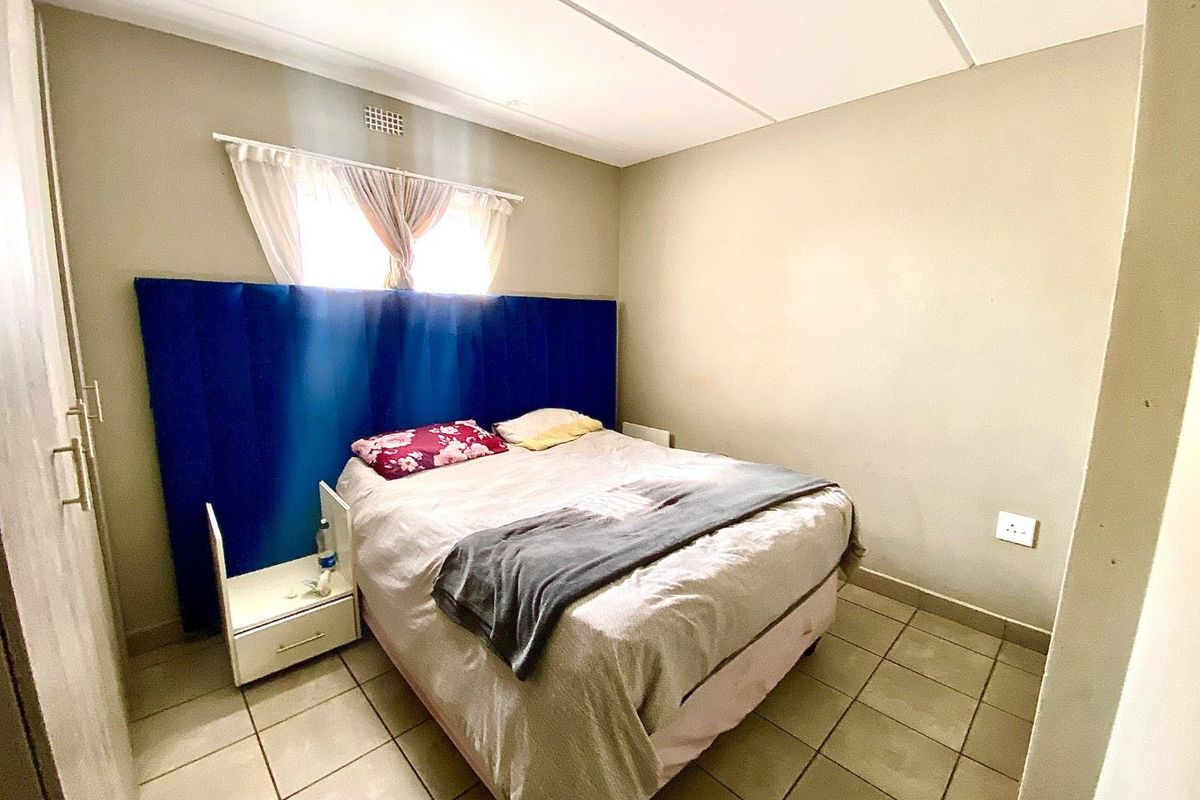 A functional bedroom featuring tiled flooring, a built-in cupboard, and a window with natural light.
