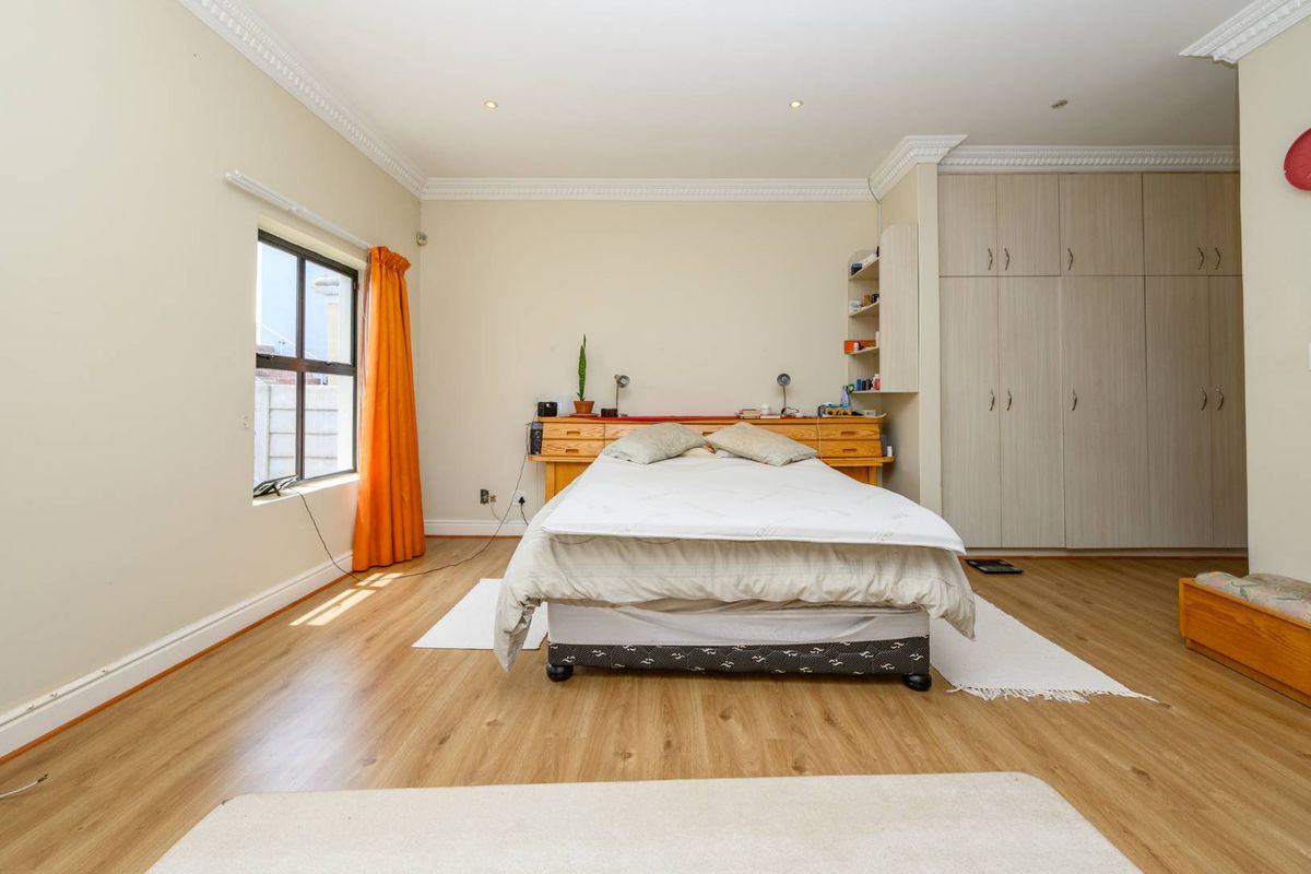 Spacious bedroom featuring light wood-look laminate flooring, extensive built-in cupboards, decorative ceiling cornicing, and recessed downlighting.