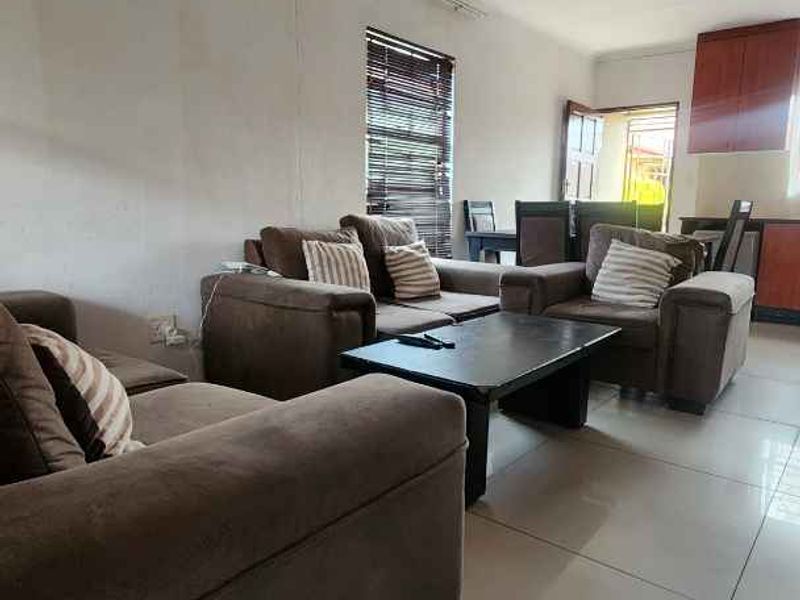 Open plan living and dining area featuring tiled flooring, neutral walls, and integrated kitchen cabinetry with natural light from a window with blinds.