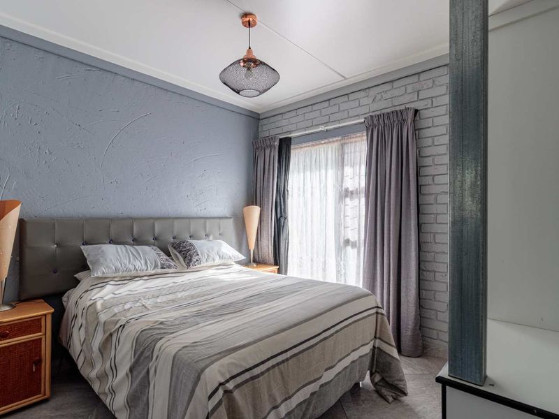 A well-maintained bedroom featuring a textured accent wall, exposed brickwork, tiled flooring, and a modern pendant light fixture.
