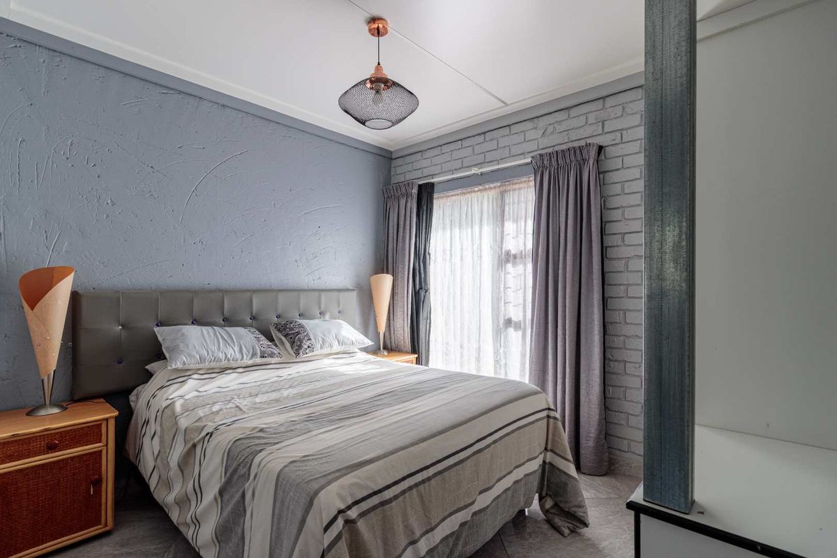 A well-maintained bedroom featuring a textured accent wall, exposed brickwork, tiled flooring, and a modern pendant light fixture.