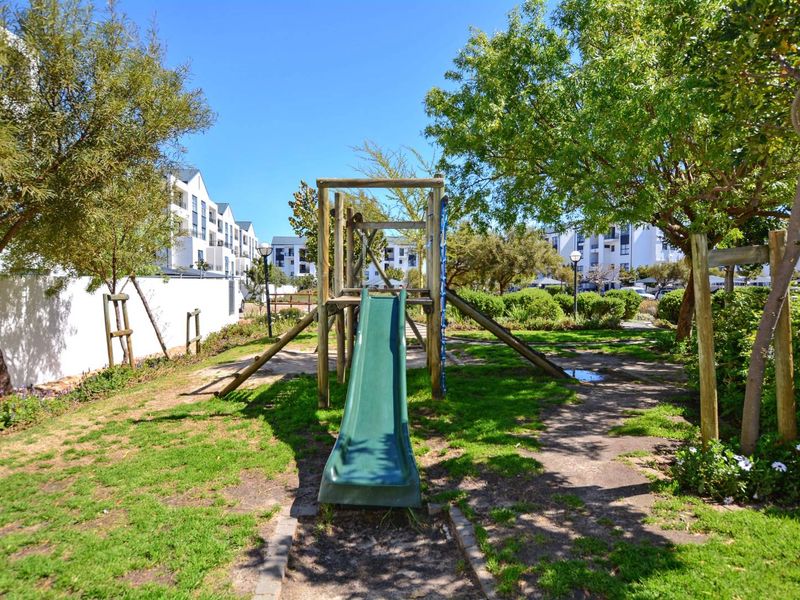 Communal garden area featuring a children's playground set, mature trees, and landscaped lawn within an apartment complex.