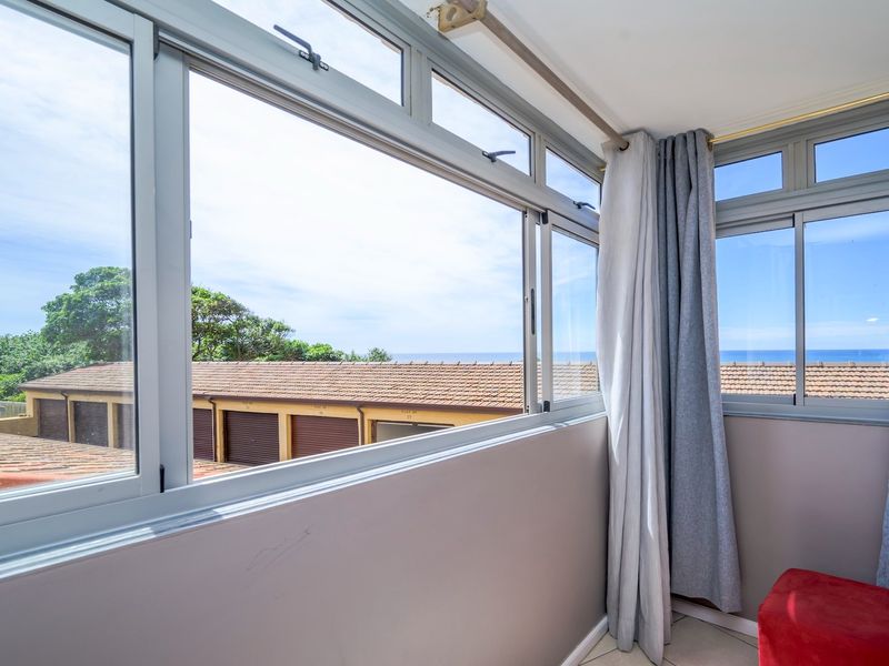 Enclosed balcony area featuring large aluminium sliding windows with views of the surrounding neighbourhood and distant ocean.