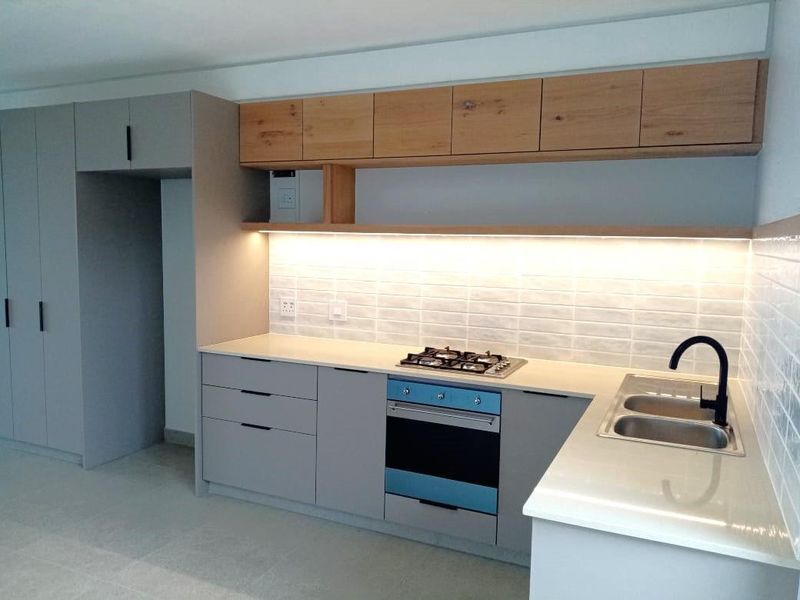 Modern kitchen featuring sleek grey cabinetry, light wood shelving, stone countertops, gas hob, built-in oven, and a stylish subway tile backsplash with integrated lighting.