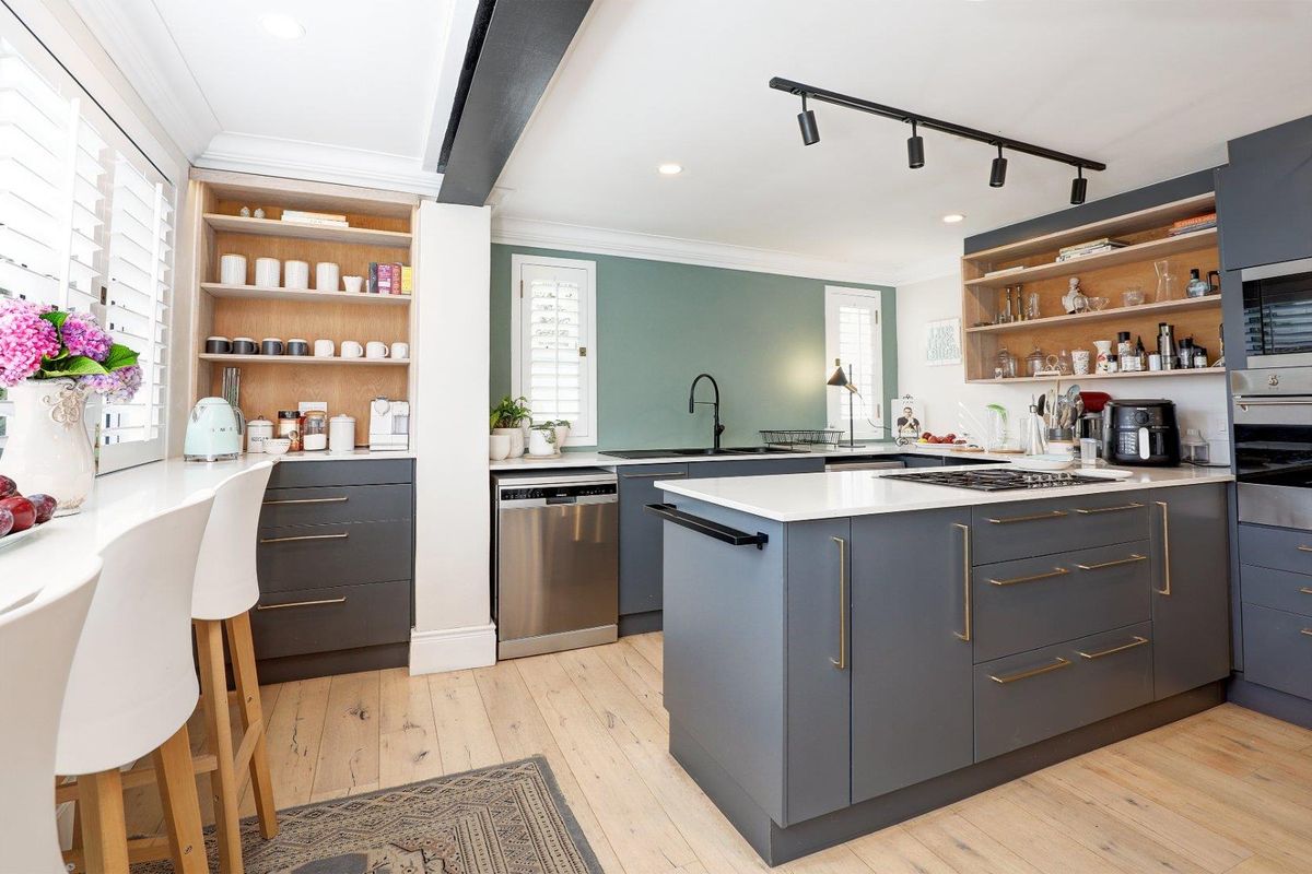 Modern kitchen featuring a central island, dark cabinetry, light wood flooring, integrated appliances, and open shelving with a stylish green accent wall.