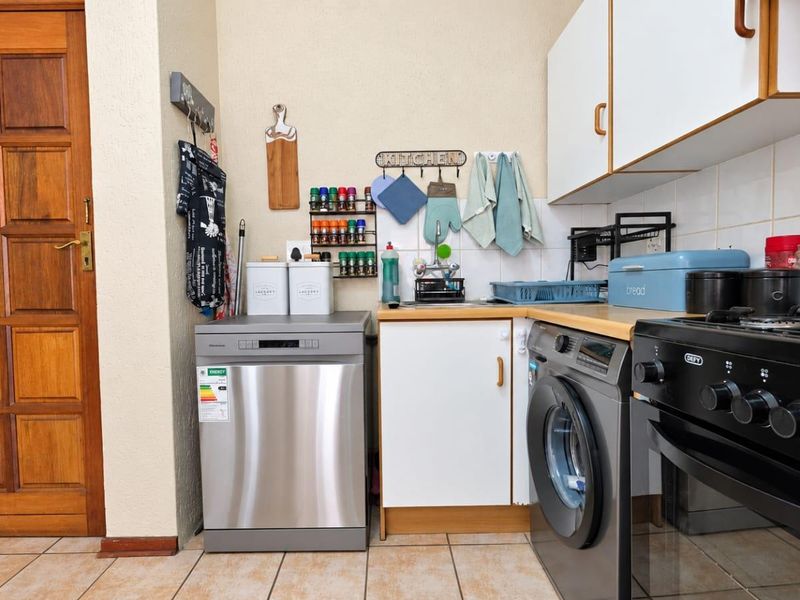 A functional kitchen area featuring tiled flooring, laminate countertops, a tiled splashback, and built-in cabinetry with space for laundry appliances.