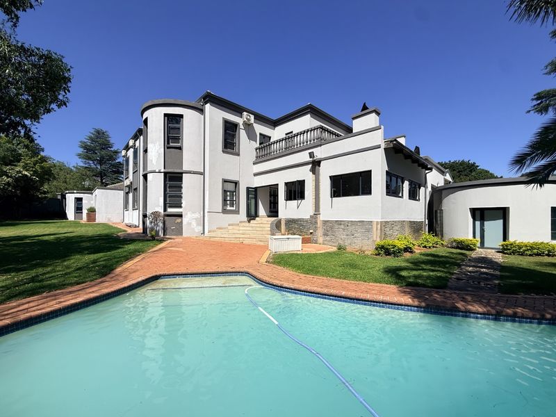 Rear view of a multi-story house featuring a swimming pool, paved patio area, balcony, and stone-clad exterior accents set within a landscaped garden.