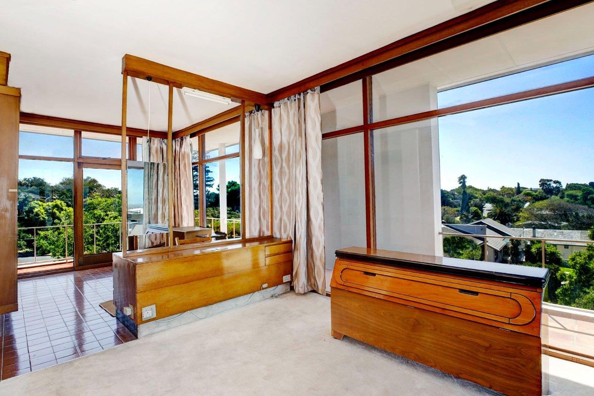 A bright bedroom featuring extensive floor-to-ceiling windows, built-in wooden cabinetry, and access to a private balcony with scenic neighborhood views.