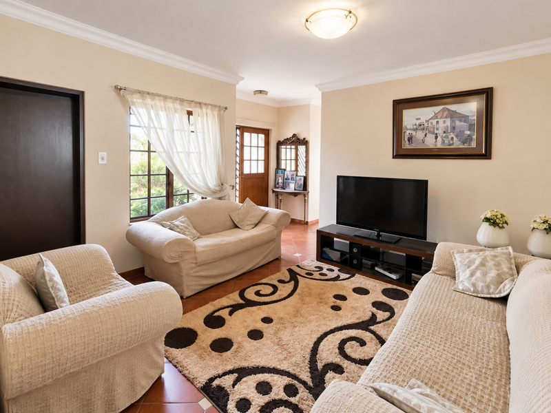 A comfortable living room featuring tiled flooring, neutral walls, and natural light through timber-framed windows, providing a warm and inviting atmosphere.
