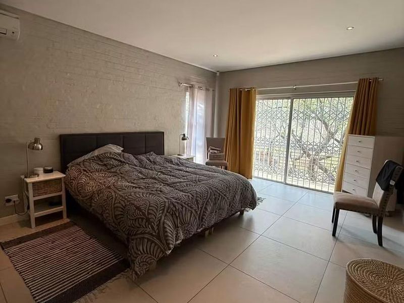 Spacious bedroom featuring large format floor tiles, an exposed brick feature wall, recessed lighting, and a sliding glass door with security gate access.